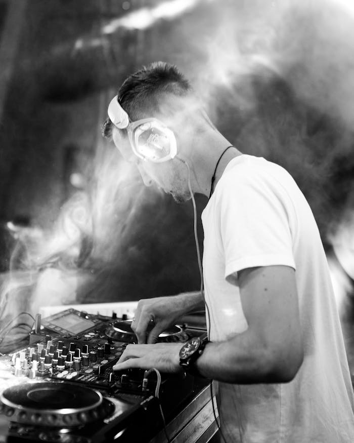 Black and white photo of a DJ mixing music with dynamic smoke effects and lighting.