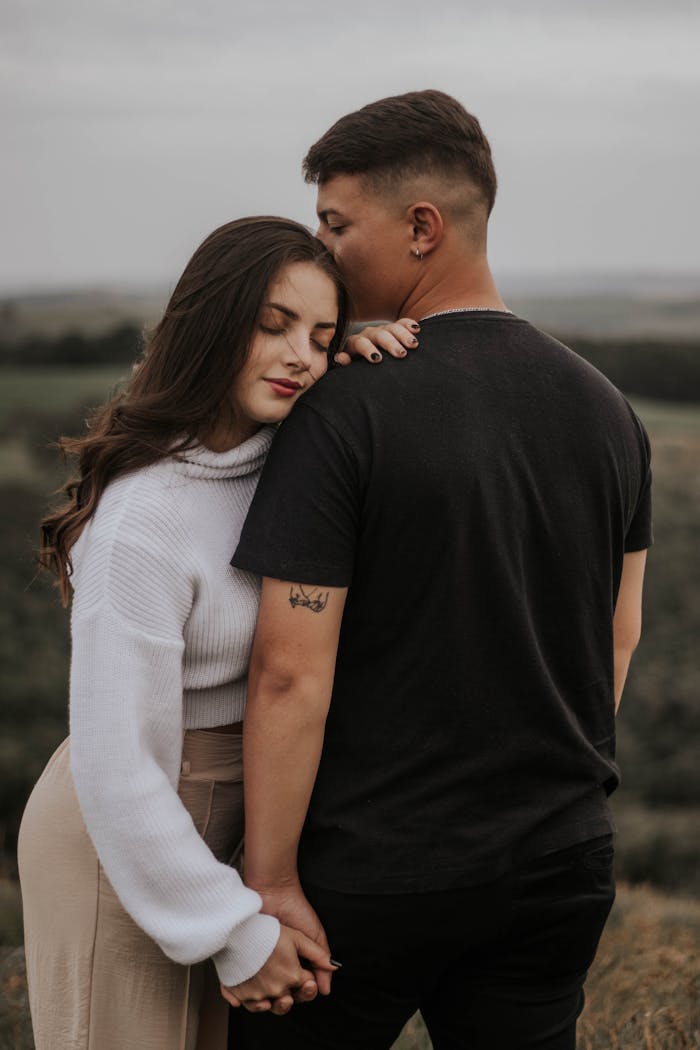 Couple standing outdoors, holding hands and embracing, creating a serene and romantic scene.