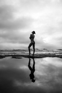 Breathtaking black and white shot of a woman by a reflective water pool under a cloudy sky.