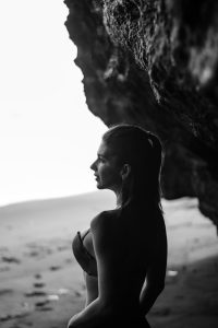 Black and white silhouette of a woman standing in a beach cave, creating a dramatic contrast.