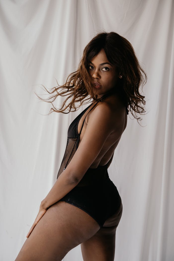 Captivating portrait of a young woman in stylish black swimwear with a seductive pose against a neutral backdrop.